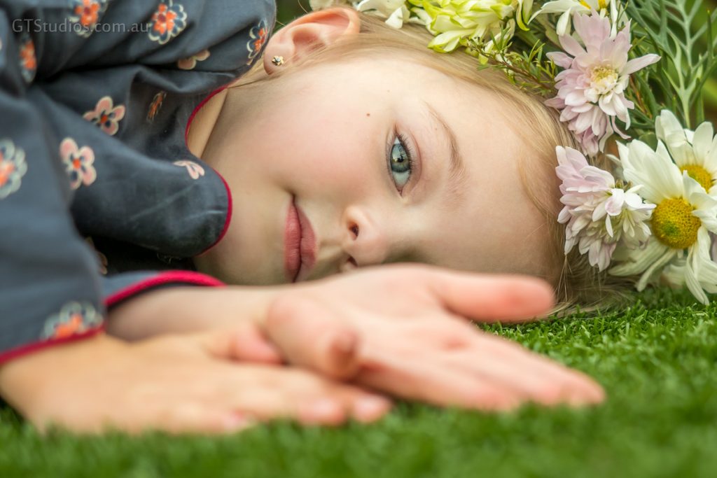 Girl laying on grass, in pretty dress with flower crown, one eye obscured